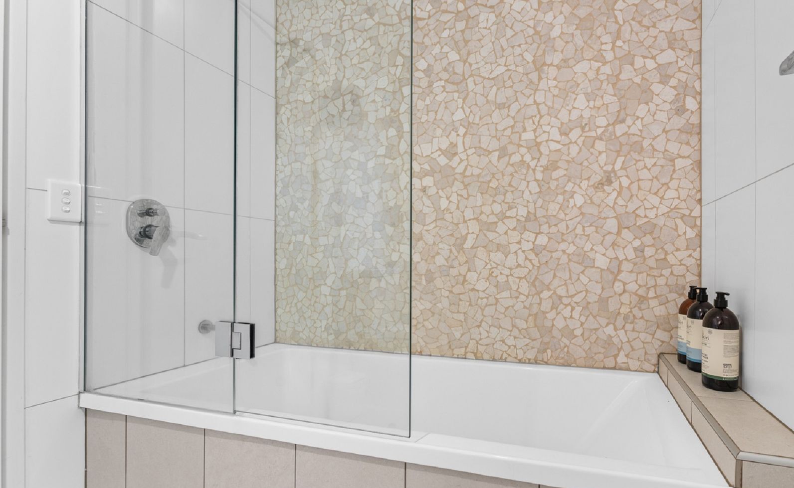 Un baño moderno con ducha envuelta en vidrio, pared de mosaicos y bañera blanca.