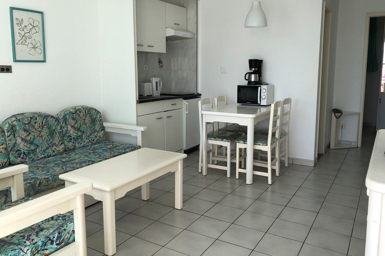 Un espace de vie compact comprenant un canapé, une table à manger avec des chaises, un coin cuisine et une lampe blanche.