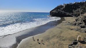 Ein Strand mit einer felsigen Klippe und blauem Himmel.