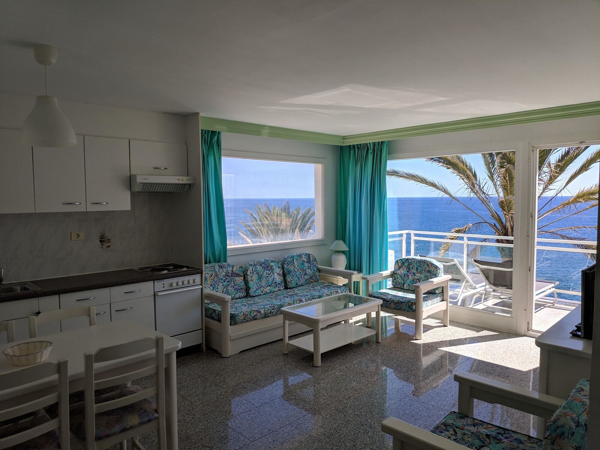 A compact living space with a kitchenette, a sofa, a coffee table, and a balcony with a view of the sea.