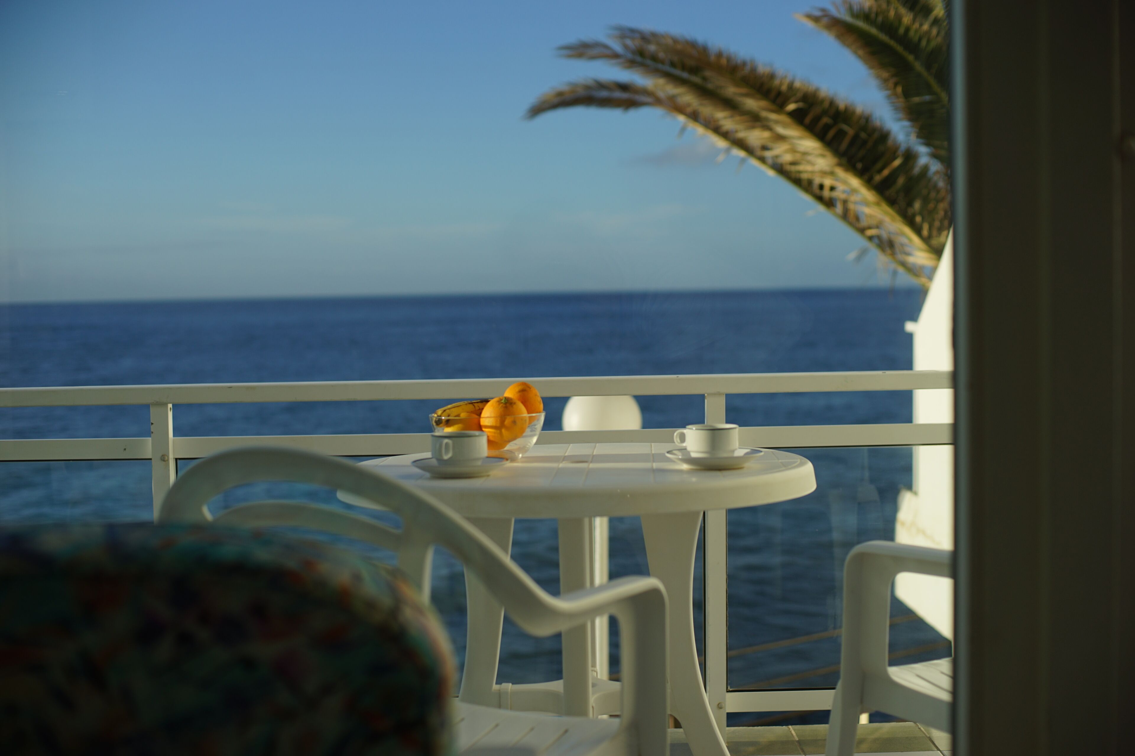 Ein Balkon mit weißem Tisch und Stühlen mit Blick auf das Meer.