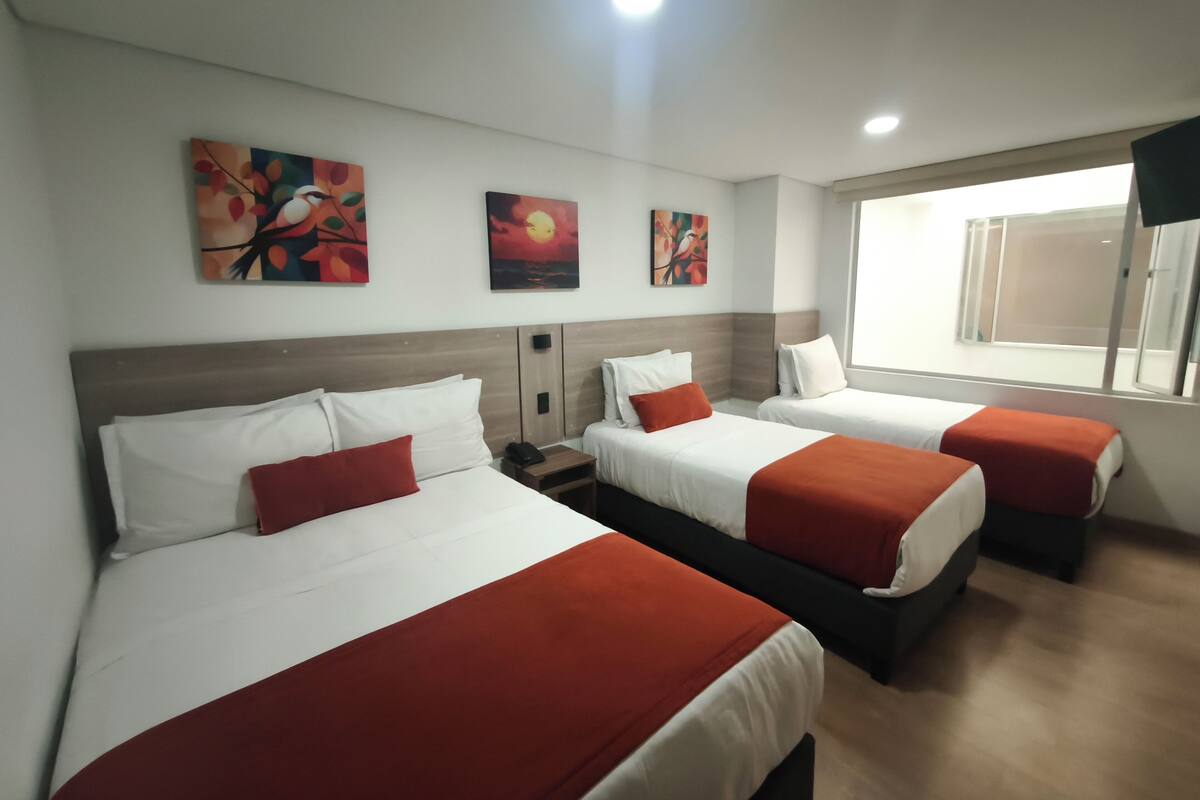 Habitació d'hotel amb dos llits, cada un amb roba de llit blanca i detalls vermells, un panell de fusta al capçal i tres quadres penjats a la paret.