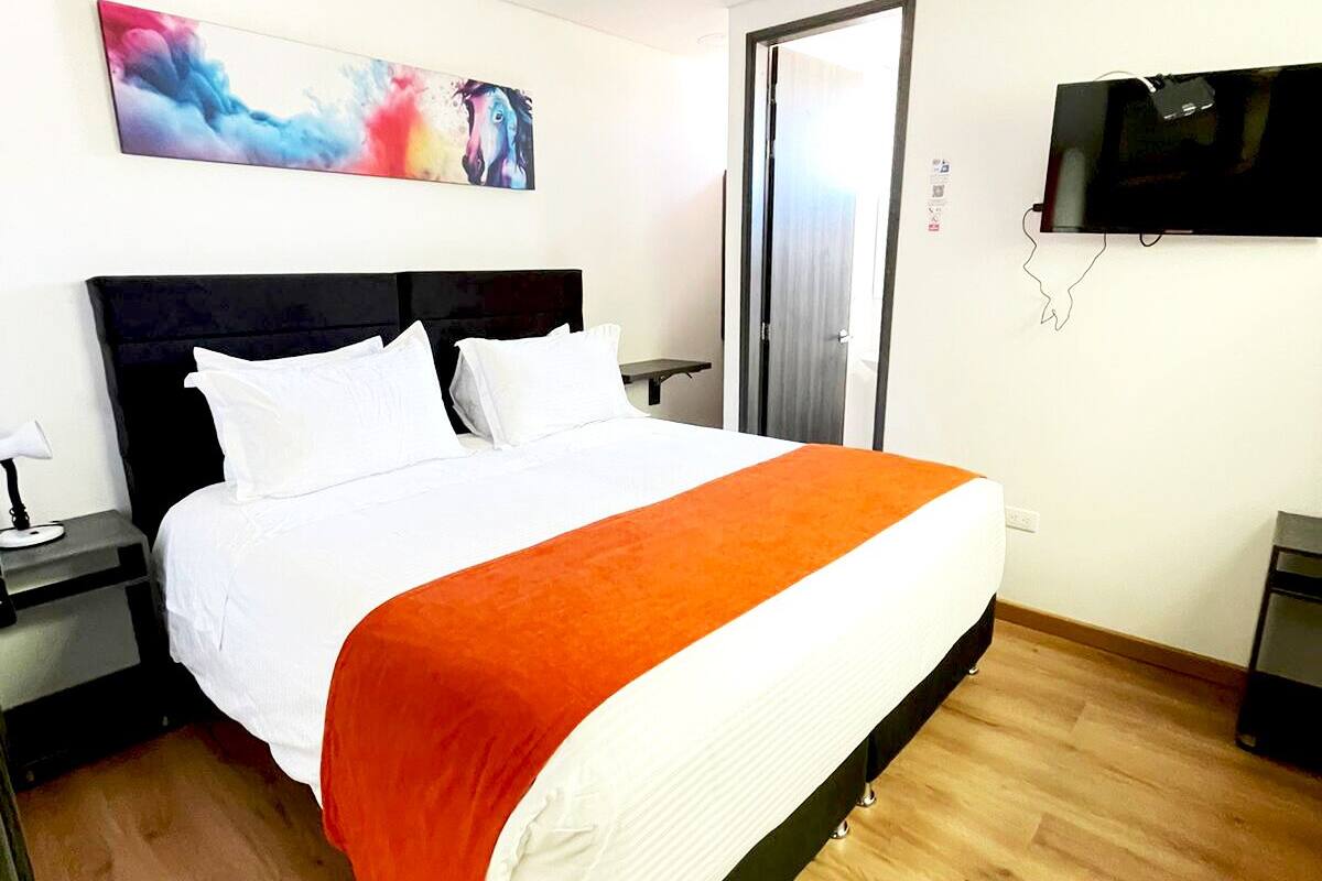 Habitació d'hotel amb llit, una taula de nit, un televisor i una porta.
