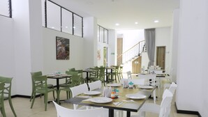 A dining area with tables and chairs, a staircase in the background, and a painting on the wall. - Hotel Portal de los Andes (Bogotá)