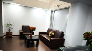 A modern living room with a brown leather sofa, a glass coffee table, and a potted plant. - Hotel Portal de los Andes (Bogotá)