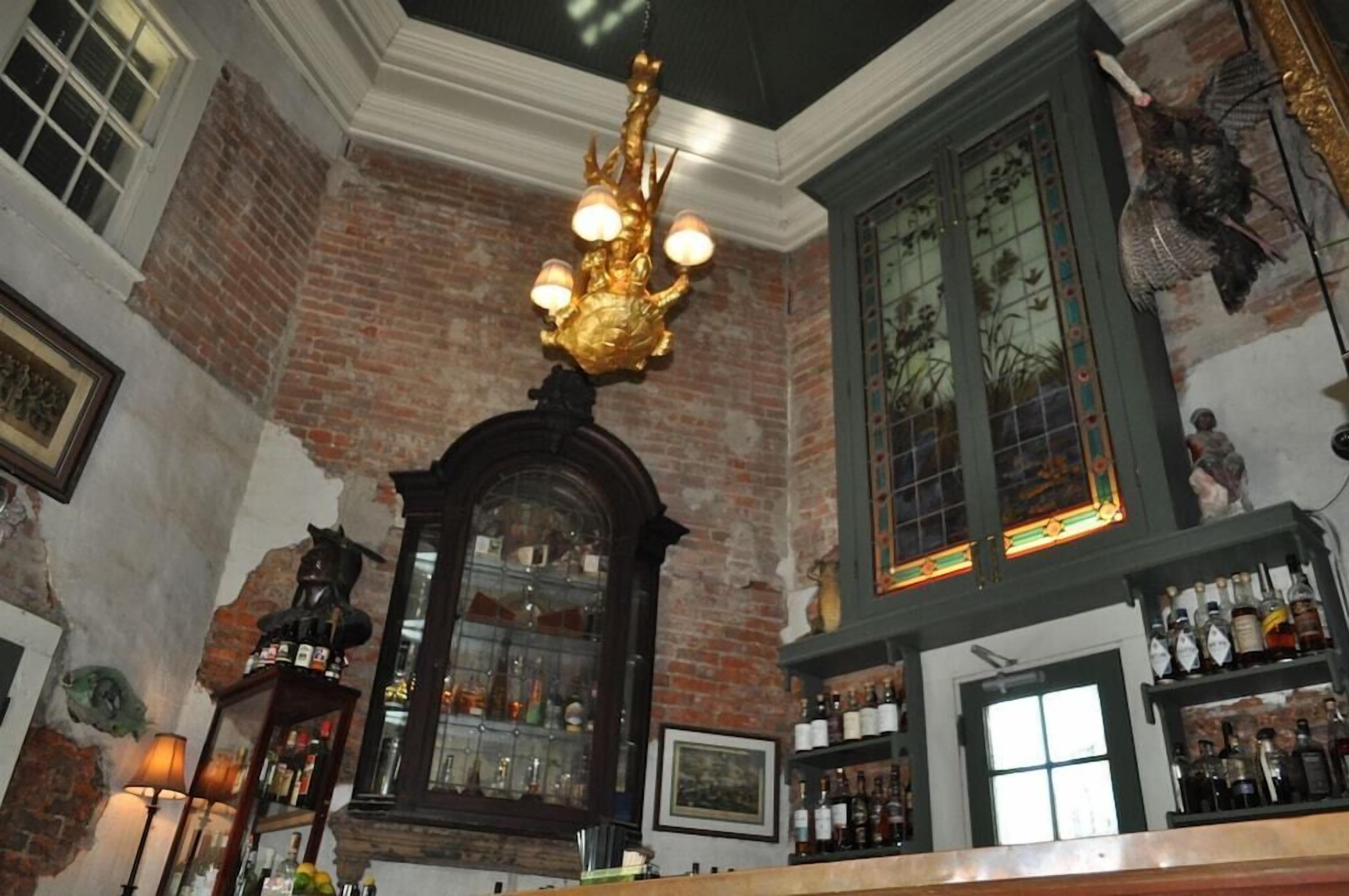 A bar area with a brick wall, a chandelier, and shelves of bottles.
