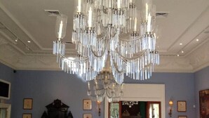 A formal dining room with a large chandelier, a piano, and a floral centerpiece on the table. - The Inn At Houmas House (Darrow)