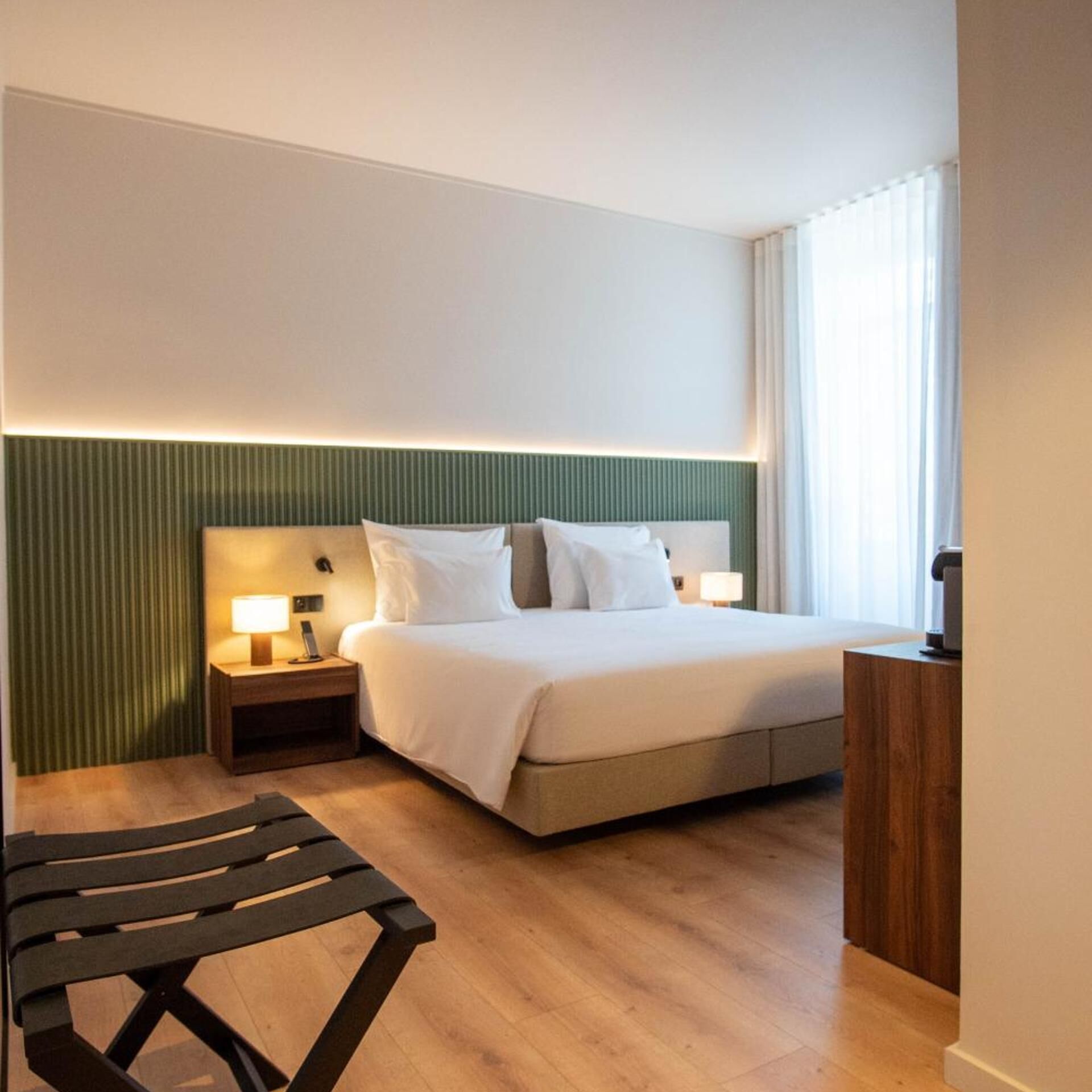 Une chambre d’hôtel avec un lit, des tables de chevet, une chaise et une vue sur l’extérieur.
