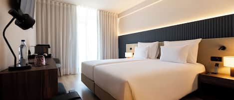 A modern hotel room with a large bed, bedside tables, a desk with a lamp, and a TV mounted on the wall.