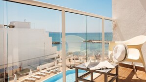 Un balcón con vista al mar, una piscina y sillas de descanso.