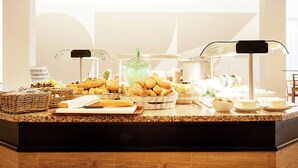 Mostrador de buffet con diversos alimentos, incluyendo pan, pasteles y una botella verde.
