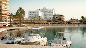 Una marina con varias embarcaciones amarradas, una playa arenosa con sombrillas y un edificio de hotel alto al fondo.