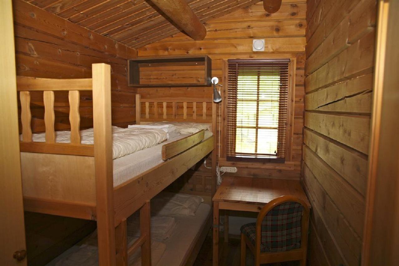 A wooden cabin room with bunk beds, a small table, and a window with blinds.
