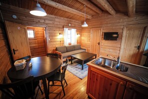 A cozy cabin interior with a dining table, chairs, a sofa, a kitchen area with a sink, and a television mounted on the wall. - Vesterland Feriepark Apartments (Sogndal)