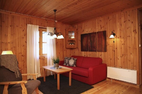 A cozy room with wooden walls, a red sofa, a wooden table, a lamp, and a radiator. - Vesterland Feriepark Apartments (Sogndal)