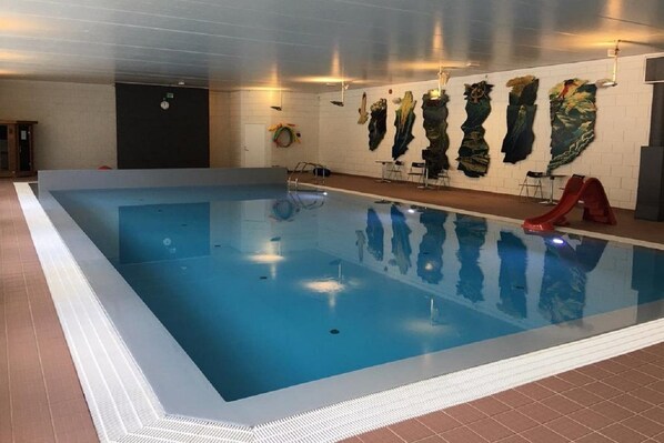 An indoor swimming pool with clear water, a slide, and wall art. - Vesterland Feriepark Apartments (Sogndal)