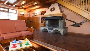 Een gezellige woonkamer met een open haard, houten balken, een bank en een salontafel.