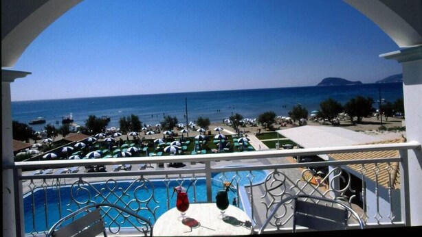 A balcony with a view of a beach and a pool. - Astir Palace (Zakynthos)