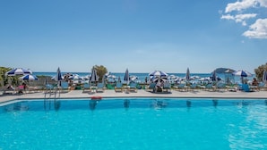 A poolside area with lounge chairs and umbrellas, a clear sky, and a view of the sea. - Astir Palace (Zakynthos)
