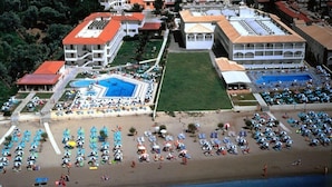 An aerial view of a coastal resort with multiple buildings, a central swimming pool, and numerous beach umbrellas. - Astir Palace (Zakynthos)