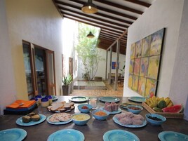 Un comedor con una variedad de platos en azul, una cesta de frutas y un cuadro abstracto y colorido en la pared.