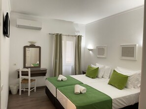 Habitación de hotel con cama, escritorio, silla, espejo y ventana con cortinas.