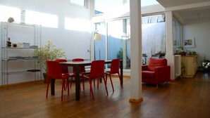 A spacious living area with a wooden floor, a dining table with red chairs, a red sofa, and a large window providing natural light. - Bright loft in the Kastanienallee (Berlin)