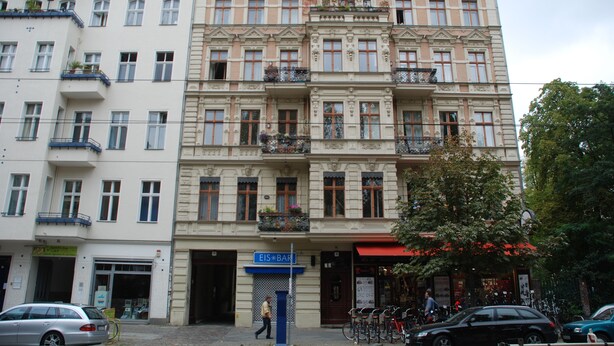A multi-story building with a classic architectural style, featuring balconies with plants and a sign for a bar. - Bright loft in the Kastanienallee (Berlin)