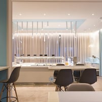 A modern dining area with a central counter, chairs, and a decorative window with vertical blinds.