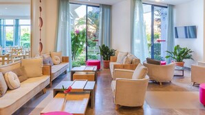 A modern hotel lobby with a sofa, chairs, a coffee table, and a TV mounted on the wall. - Albatros Hotel (Corfu)