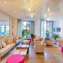 A modern hotel lobby with a sofa, chairs, a coffee table, and a TV mounted on the wall.