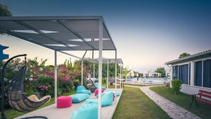 A covered outdoor seating area with bean bags and a hanging chair, a pool, and a building with large windows. - Albatros Hotel (Corfu)