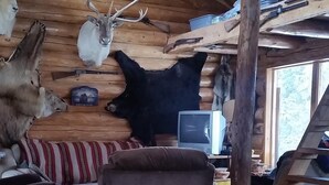 L’intérieur d’un chalet rustique, avec des murs en bois, une table à manger, des chaises, un canapé et des têtes d’animaux fixées au mur.