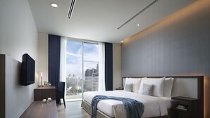 Une chambre d’hôtel moderne dotée d’un grand lit, d’un téléviseur à écran plat fixé au mur, d’une table de chevet avec une lampe et offrant une vue sur la ville grâce à de grandes fenêtres.