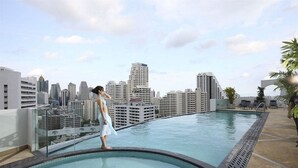 Une piscine sur le toit offrant une vue sur la ville, avec une rambarde en verre et des chaises longues.