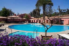 A swimming pool surrounded by palm trees and purple flowers, with a building in the background. - Wyndham Costa del Sol Arequipa (Arequipa)
