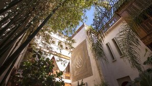 An indoor courtyard with traditional architecture, including a decorative wall with calligraphy, surrounded by lush greenery and bamboo. - Riad Flam (Marrakech)