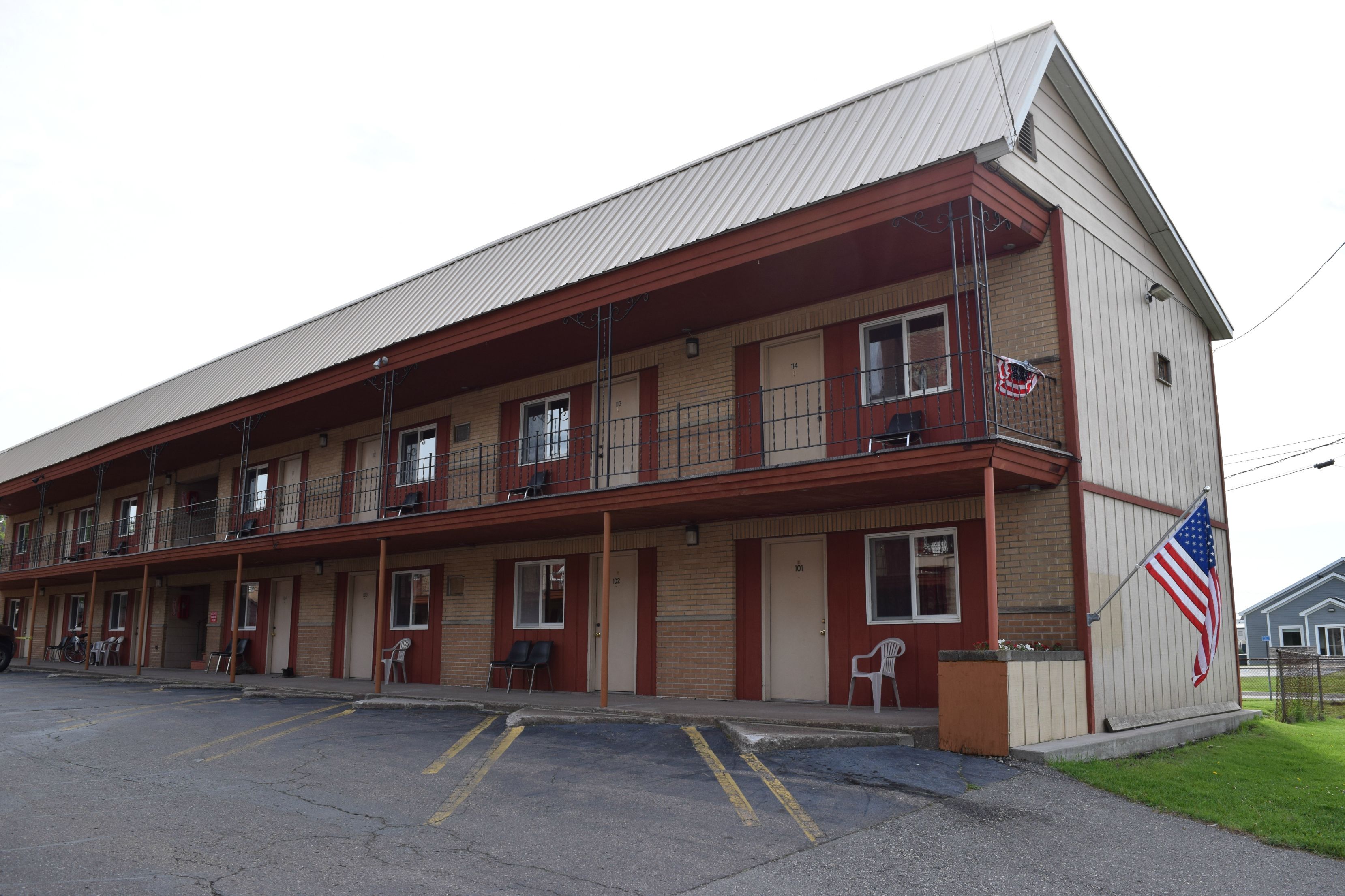 A two-story motel with a red and beige exterior, multiple rooms, and an American flag on the side.