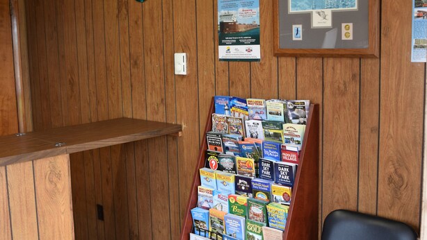 A reception area with a wooden wall, a framed picture, a bulletin board with brochures, and a black chair. - Mid-City Motel (Sault Ste. Marie)