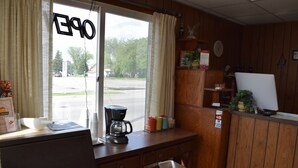 A room with a desk, a coffee maker, a trash bin, and a window with curtains. - Mid-City Motel (Sault Ste. Marie)
