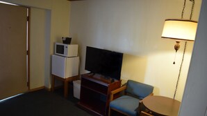 A compact hotel room with a television, a small refrigerator, a desk with a lamp, and a chair. - Mid-City Motel (Sault Ste. Marie)