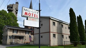 A Mid-City Motel with a signboard, a flag, and a building with a flat roof and multiple windows. - Mid-City Motel (Sault Ste. Marie)