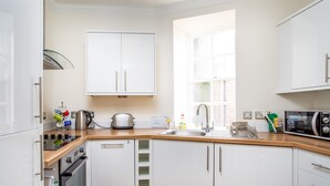 A modern kitchen with white cabinets, a wooden countertop, a built-in oven, a microwave, and a window providing natural light. - Advocates Close (Edinburgh)