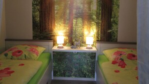 A bedroom with two beds, each with floral bedding. There are two lamps on a bedside table, and a large forest mural on the wall. - Pure resin romance; Time out for 2 persons; feel good and relax (Altenau)