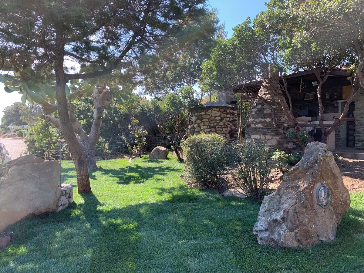 Una casa de piedra con chimenea de piedra, rodeada de un césped cuidado y grandes rocas.