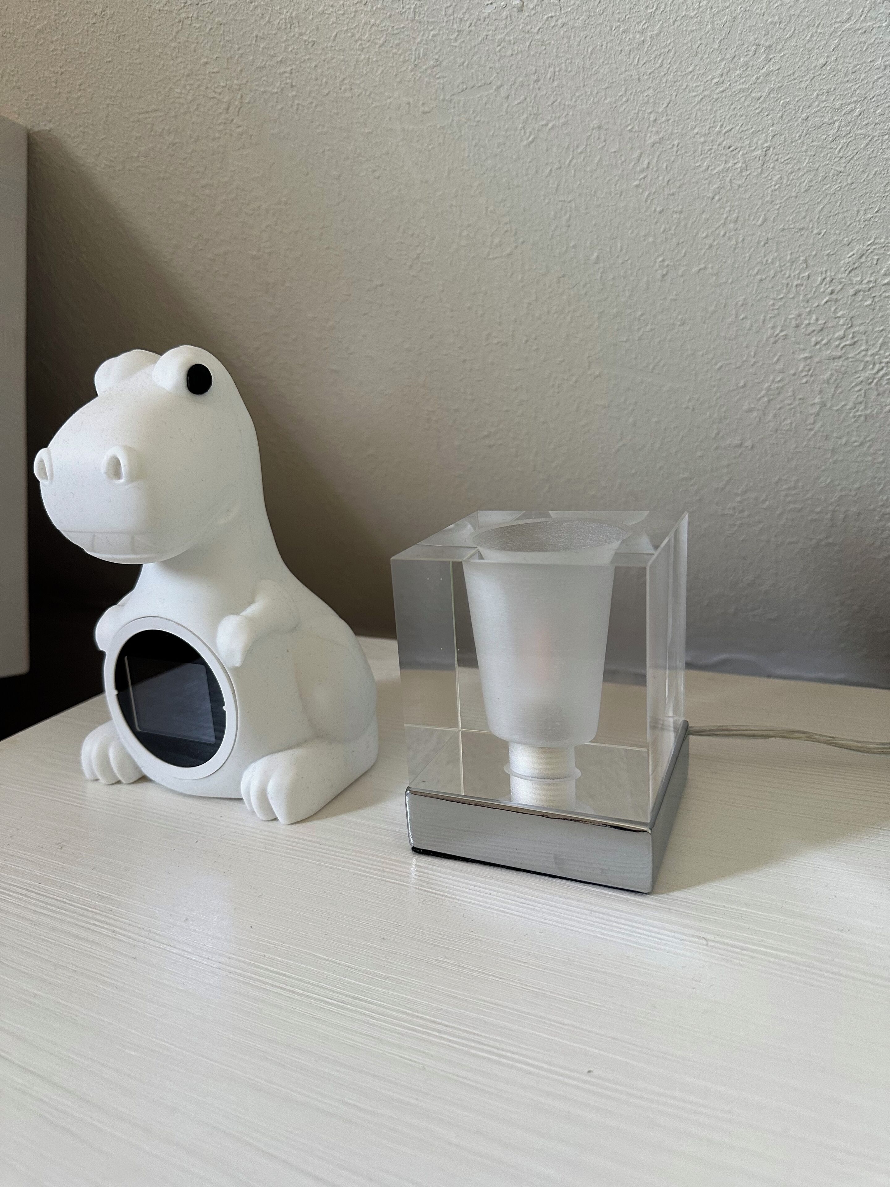 A white ceramic frog figurine and a clear glass vase with a white base on a white surface.
