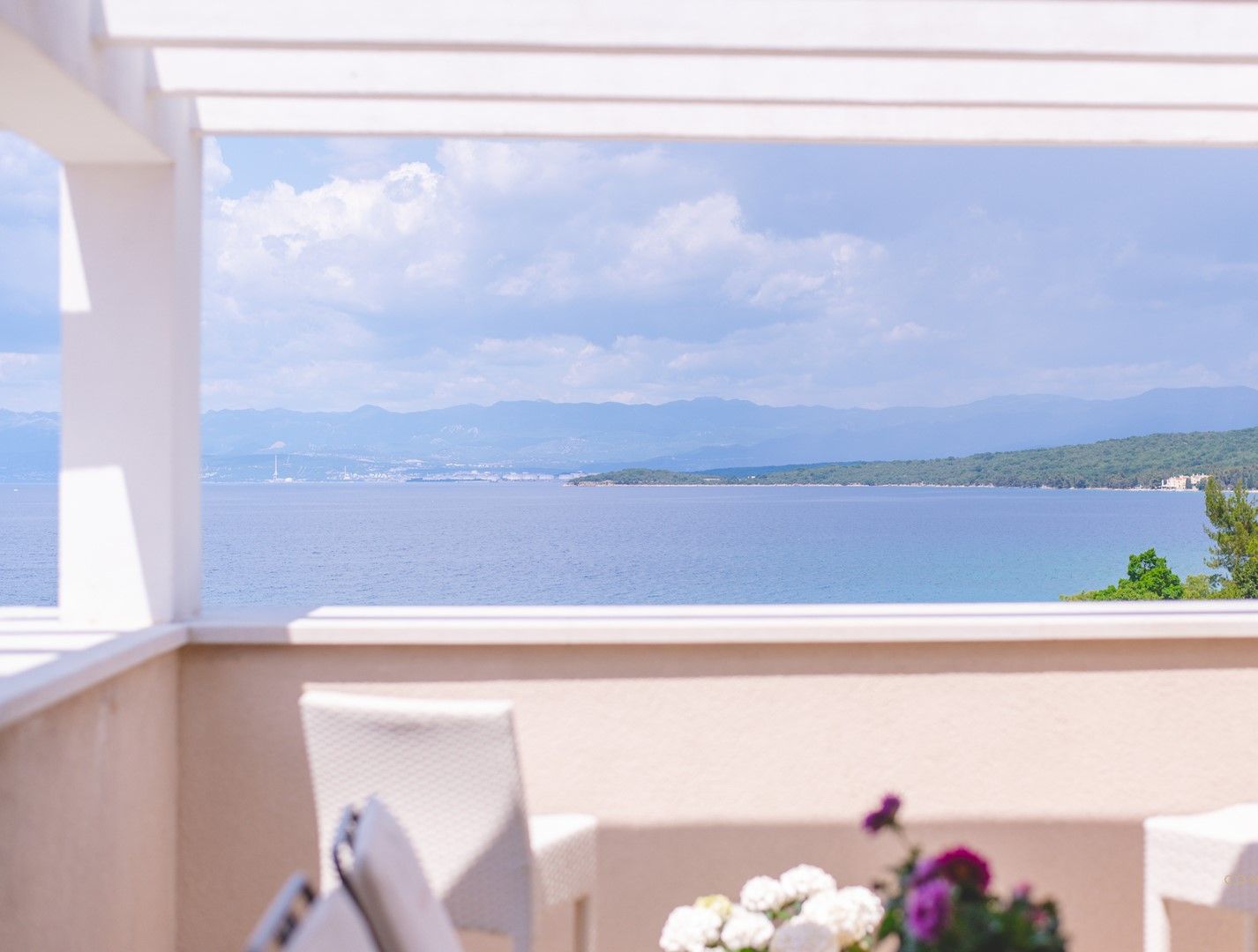 Un balcón con vista a un mar tranquilo y montañas distantes.