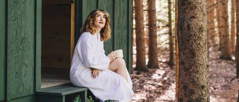 A person sitting on a wooden bench outside a cabin with a forest backdrop.