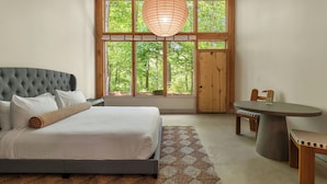A bedroom with a large bed, a wooden ceiling, a window with a view of trees, and a small table with chairs. - The Fields of Michigan (South Haven)