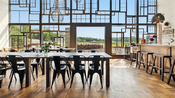 A spacious dining area with a large table and chairs, a bar area, and large windows offering a view of the outdoors. - The Fields of Michigan (South Haven)